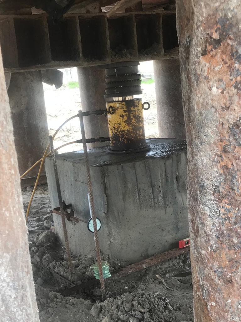 Close-up of a hydraulic jack applying load to a concrete pile cap between piles