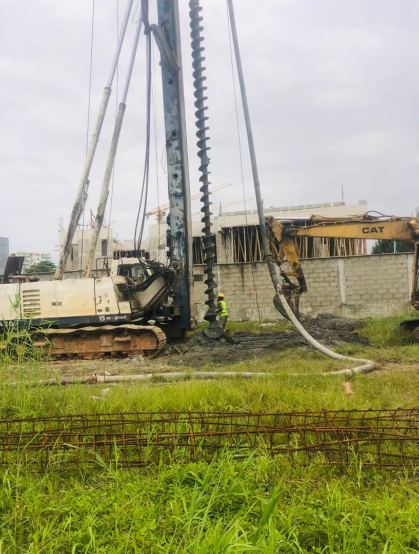 CFA auger piling rig with concrete pump line and CAT excavator beside a building under construction