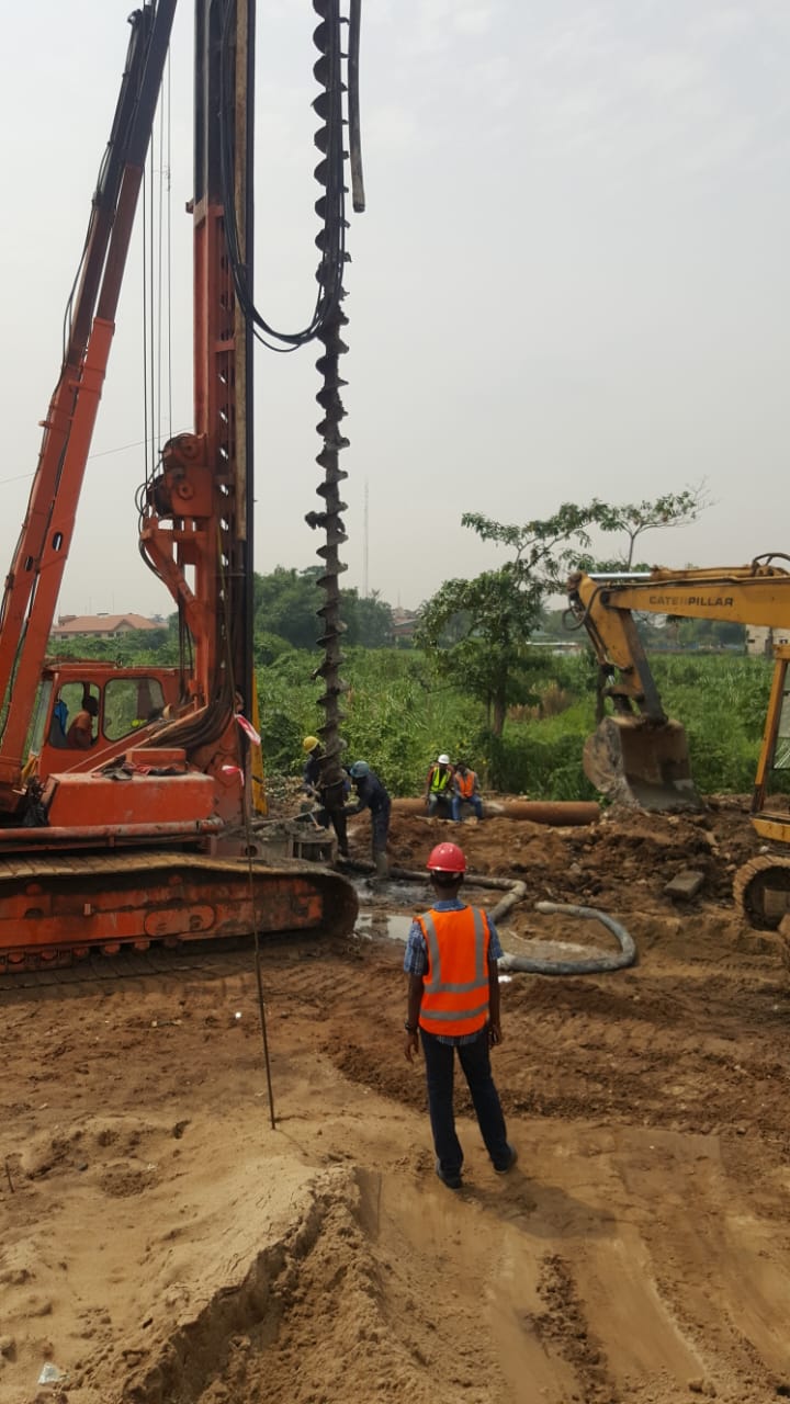 Rotary piling rig, excavator and crew working on a cleared greenfield site