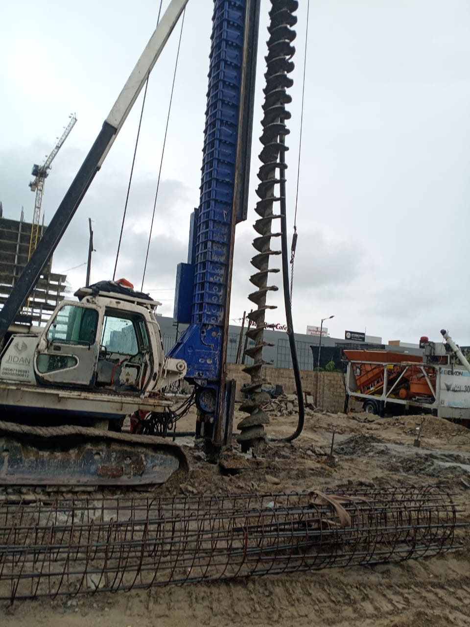 CFA auger piling rig with reinforcement cages and a mobile batching plant on site