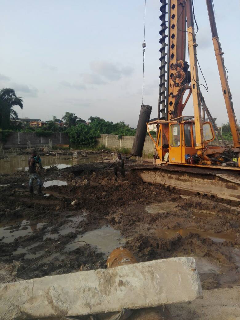 Piling rig lowering a casing into soft ground during foundation works