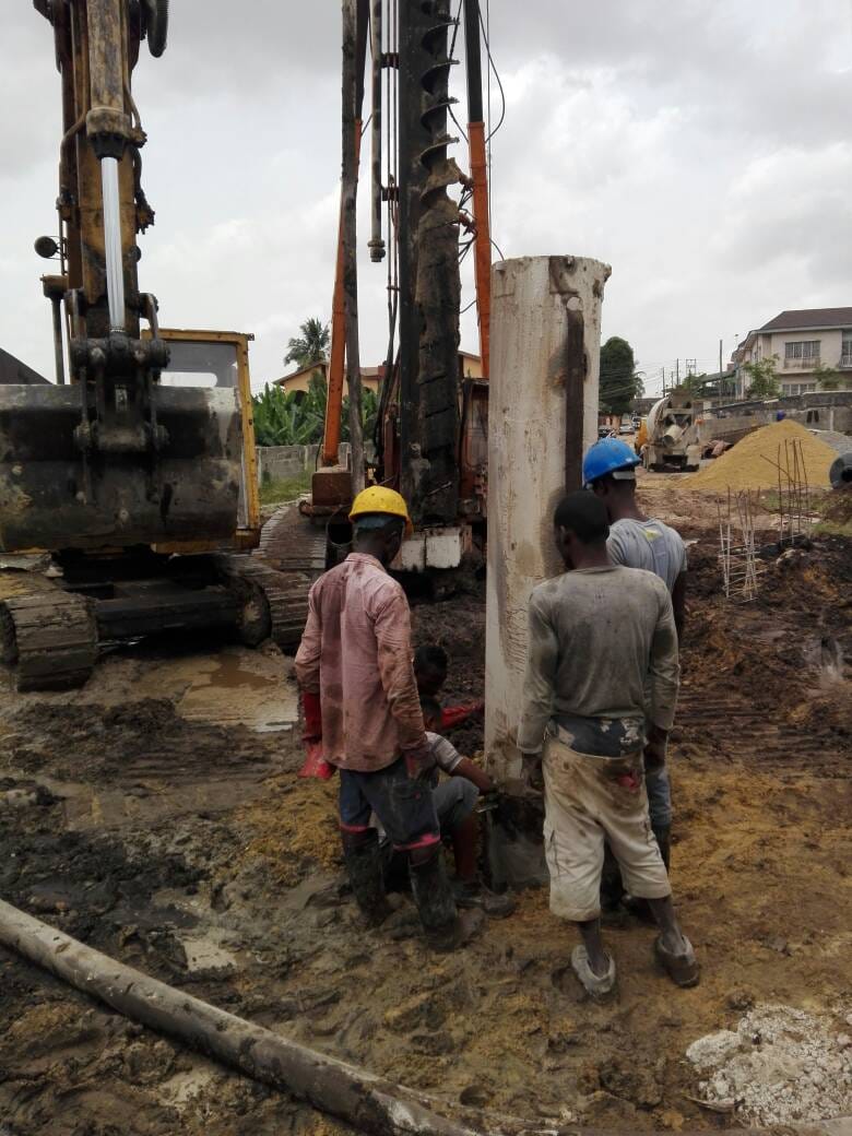 Crew installing a steel pile casing with an excavator and concrete truck on site